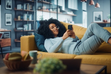  Person laying on couch relaxing while browsing on the phone. 