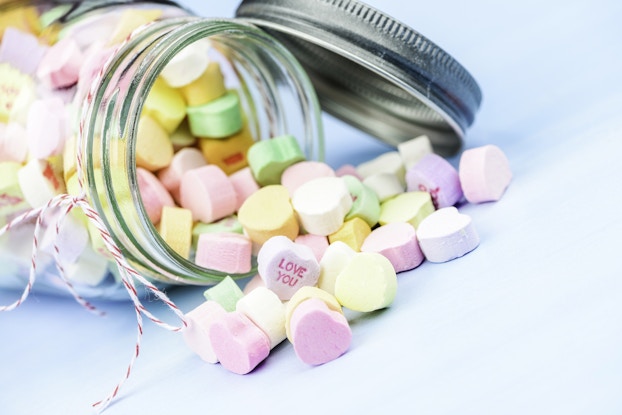 Candy hearts for Valentine's Day pouring out of a jar on its side.