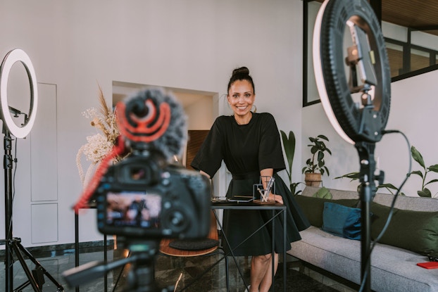  A businesswoman wearing a black dress smiles at the viewer while she records a video product demonstration.