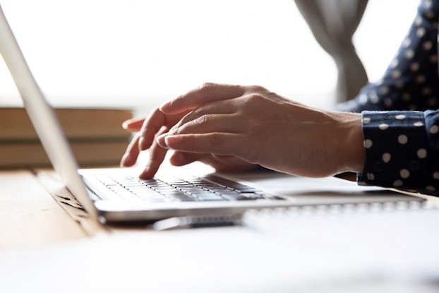  A close-up of someone's hands typing on a laptop keyboard. Most of the person in the picture is out-of-frame, but it can be seen that they are wearing a dark blue shirt with white polka dots.