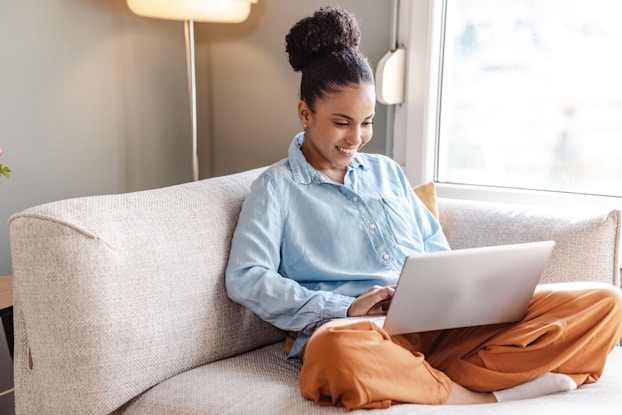 Woman sitting on her couch while working on her laptop.
