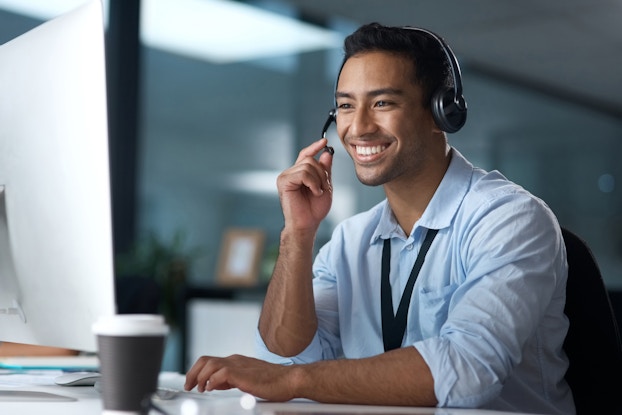 Happy man sitting at a desk on a computer wearing a headset.