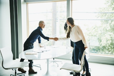  Two coworkers shaking hands in a bright, open office. 