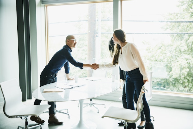 Two coworkers shaking hands in a bright, open office.