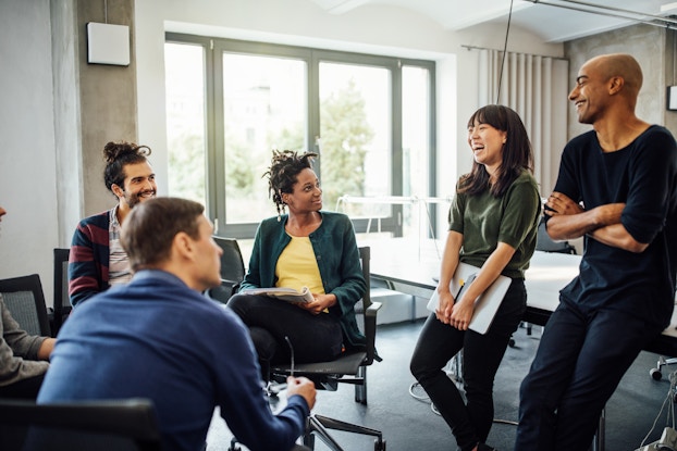  Group of diverse colleagues sitting in a circle and laughing together.