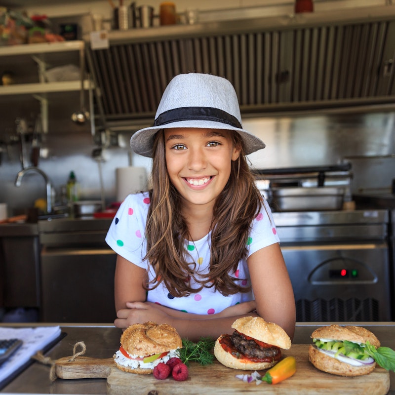 Young girl standing in a kitchen in front of three sandwiches.