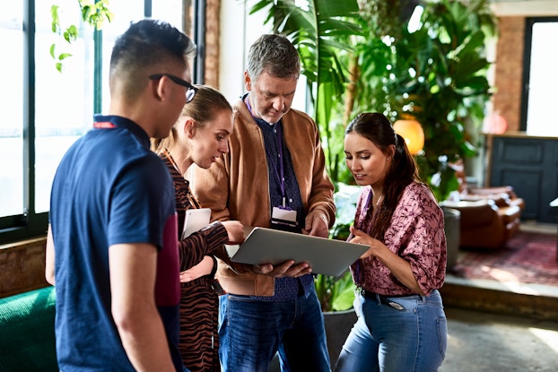 Team of four coworkers standing huddled around a tablet.