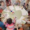 a group of children sitting at a round table painting