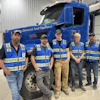 a group of men standing in front of a blue truck