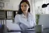 A woman business manager is holding a paper with her right hand and double-checking data against the data displayed by her laptop computer's screen.